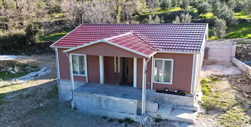 Aerial view of the finished single-storey prefab house with a red tiled roof and covered front porch on a hillside plot