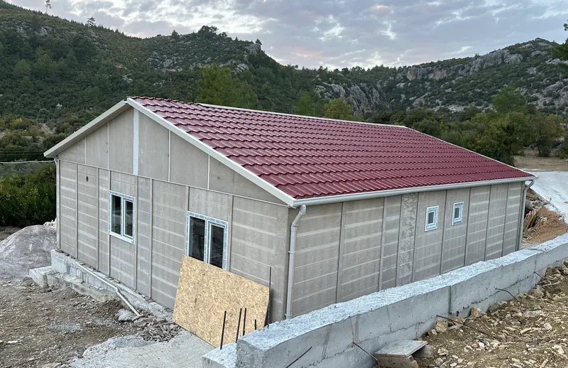 Prefab panel house assembled on its foundation, roof on, before exterior finishing