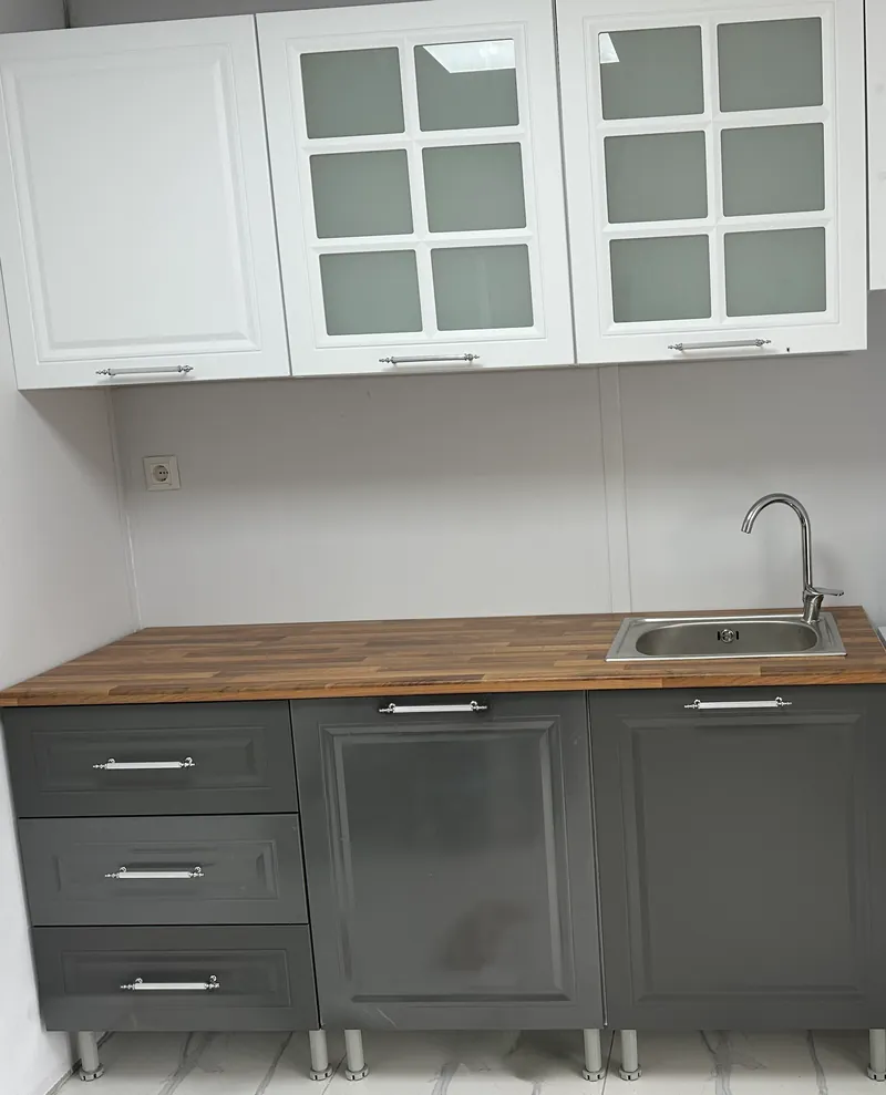 Compact kitchen with white glazed wall cabinets, grey base units and a wood worktop with sink