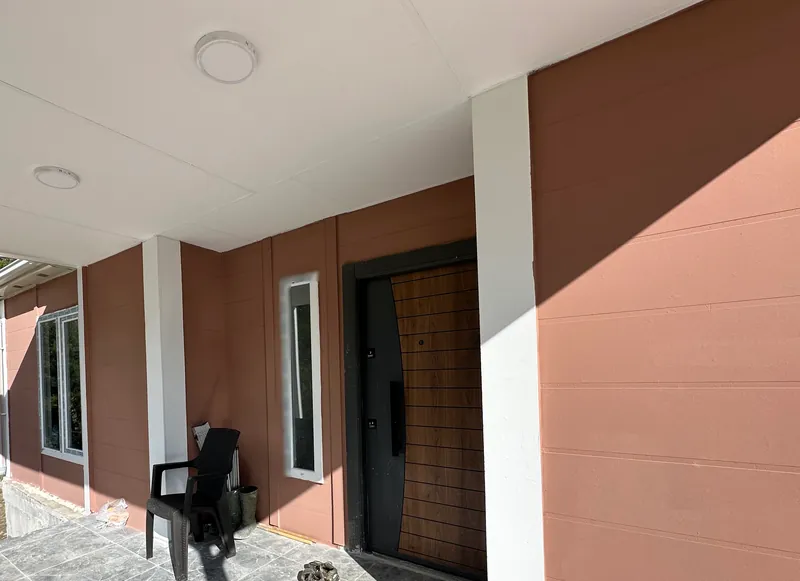 Covered porch with marble-look tiles, a wood-panel front door and a narrow side window